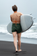 Rear view of unrecognizable woman surfer walking on sand beach with surfboard in hand