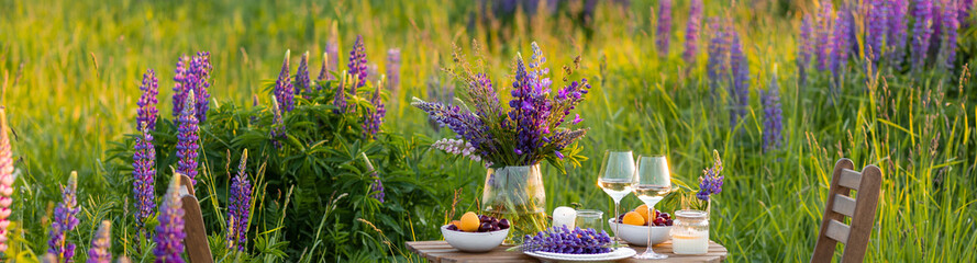 Beautiful countryside wedding of romantic dinner decor on blooming meadow with purple violet lupins...