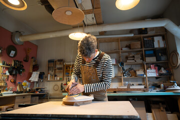 Sanding wood with orbital sander at workshop. Focused man carpenter polishes wooden seat of a...