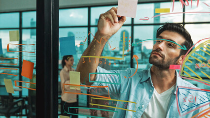 Professional businessman uses sticky notes at glass wall with graph to brainstorming idea while...