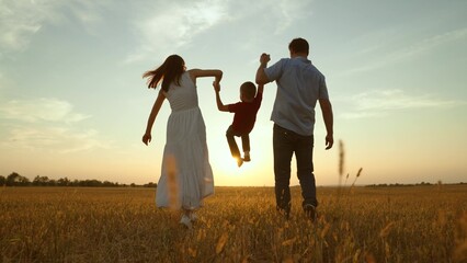 Mom dad kid hold hands at sunset. Joyful merry happy family together kid child boy playing jumping...