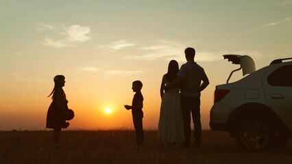 Family at sunset by car in field silhouettes. Children kids plays ball parents hugging enjoying...