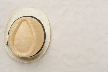 Straw hat on sand background, top view
