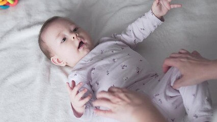 Mother playing in bed with her 6 month old baby daughter, baby girl laughing and moving with joy