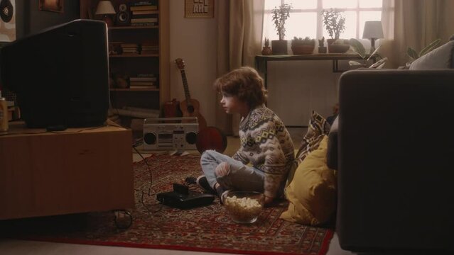Side full handheld footage of Caucasian millennial boy plugging video cassette into console and starting playing arcade game on tube TV at home alone in 90s