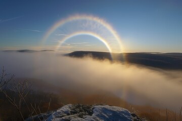 Majestic sunrise with atmospheric halo effect over a layer of fog enveloping mountainous terrain, serene nature moment