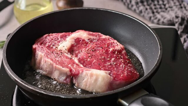 raw steak meat with pepper is cooking on a pan in heated oil, the process of cooking a steak