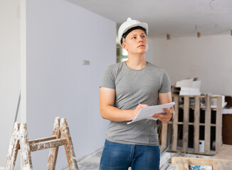 Teenage young man in hardhat doing errand in apartment during repair works, checking project...