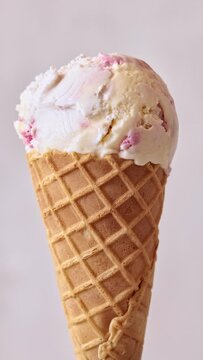 Ice cream cone close-up. Pink Icecream scoop in waffle cone rotated over light background.  Vanilla and strawberry or raspberry flavor Sweet dessert, rotation closeup. 4K