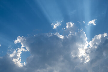 Sunbeams radiating through silver lined clouds in a vivid blue sky. Ideal for concepts of hope and...