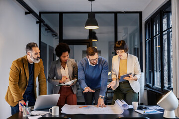 Multicultural architects discussing blueprints at meeting room on a briefing.