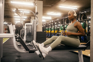 A strong black sportswoman with headphones practicing backs on cable machine at gym.
