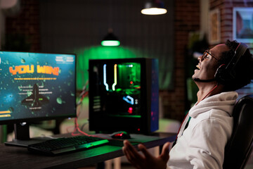 Excited gamer celebrating winning online multiplayer futuristic videogame match. African american man enjoying leisure time at home, feeling ecstatic about gaming championship victory