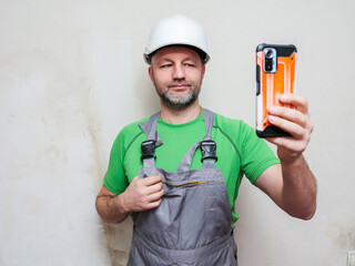 Portrait of a construction worker on light wall background. Builder in grey heavy duty clothes,...