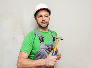 Portrait of a construction worker with tools on light wall background. Builder in grey heavy duty...