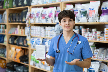 Experienced veterinarian young man is standing in pet store with pack of food in hands. Specialist...