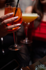 A woman holds a cocktail in her hand, with her fingers wrapped around the glass