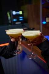 A woman holds a cocktail in her hand, with her fingers wrapped around the glass
