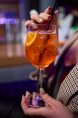 A woman holds a cocktail in her hand, with her fingers wrapped around the glass