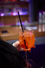 A woman holds a cocktail in her hand, with her fingers wrapped around the glass