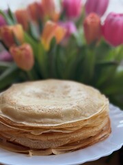 A stack of homemade pancakes sits on a plate, golden and tempting, with a blur of colorful tulips in the background, hinting at a cozy brunch.