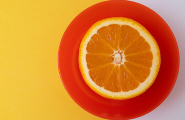 A slice of orange is on a red plate. The orange is cut in half and the plate is yellow