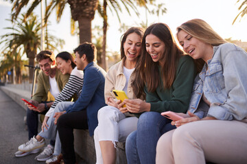 Large and diverse group of generation z friends smiling sitting on street using and looking mobiles phones. Addiction of technology and social networks of young happy people sunny day outdoors