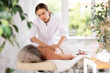 Obraz na płótnie Canvas Unrecognizable elderly woman lies face down on massage couch and enjoy spa treatments for body care. Gentle massage of problem areas, prevention of back pain, relief of fatigue