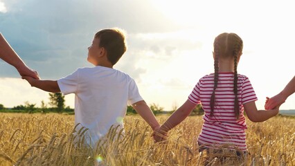 Smiling little boy and girl holding hands parents going at sunny sunset natural dry wheat field...