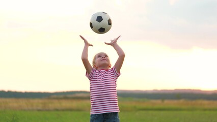 Laughing little girl playing football ball at summer sunset field enjoy happy childhood. Smiling...
