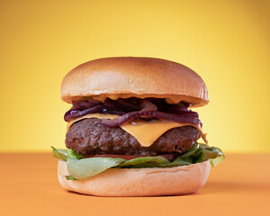 Juicy Cheeseburger with Lettuce, Tomato and Onions on a yellow and orange background