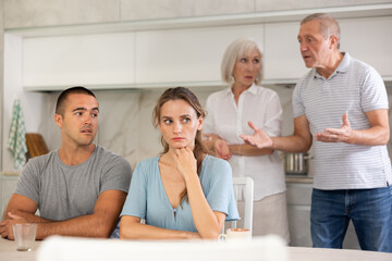 Portrait of an offended married couple in a home kitchen, which mature family members reprimand. Family conflict