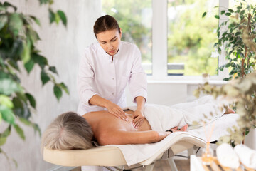 Middle-aged woman actively rubs shoulders and back of elderly female during general back massage procedure.