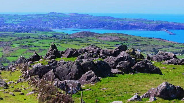 Aerial shot travelling over high rocky peak of mountain to reveal farmland and coastal port of Fishguard in Wales.