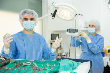 Confident young male veterinarian standing in full surgical outfit and sterile gloves in veterinary...