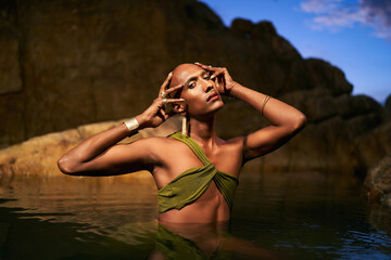 Androgynous bipoc lgbtq model poses in water inside natural pool at night. Non-binary person shows...
