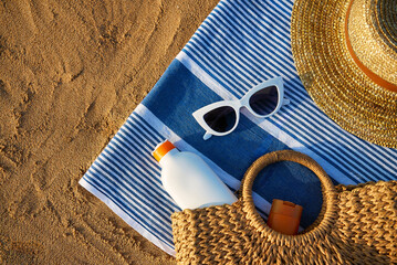 Summer beach essentials laid on sand for sun protection. Straw hat, white sunglasses, sunscreen...