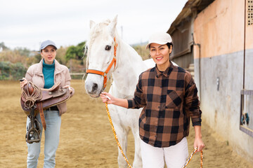 Two women jokey preparing a horse for riding in paddock