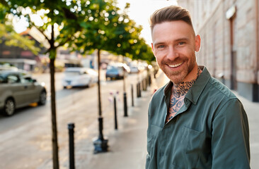 A tattooed smiling man at sunrise or sunset looking at viewer.