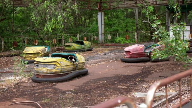 Abandoned car attraction in the city of Pripyat. The whole playground was overgrown with greenery and trees. Consequences of the Chernobyl disaster.