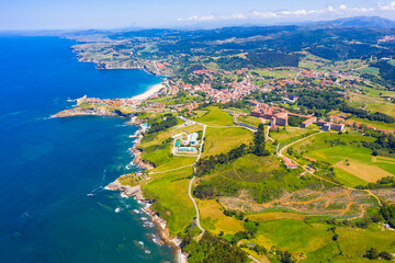 Picturesque aerial view of green valleys on Cantabrian Sea coastal area with brownish roofs of houses of Comillas village, Spain..