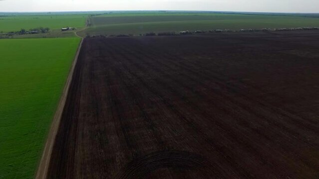 The drone makes a panorama over a beautiful green and brown field at a bird's eye view. You can see the horizon line and the blue sky with white clouds.