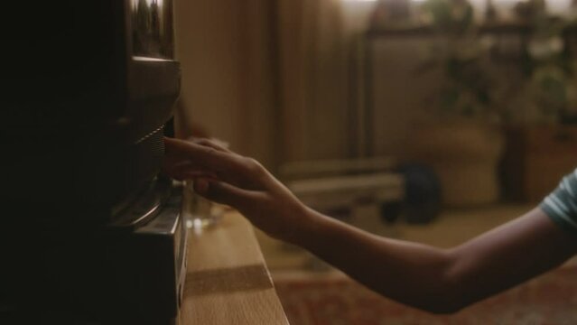 Side handheld footage of naughty gen Y African American boy taking cassette out of schoolbag, putting it into tape video recorder and switching on retro TV watching horror movie while alone at home