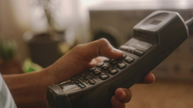 Side closeup of anonymous person dialing number on retro handset in room with softlight with nostalgic atmosphere
