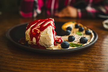 Meringue roll with jam and blueberries on black plate.