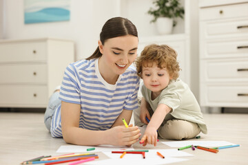 Mother and her little son drawing with colorful markers on floor at home
