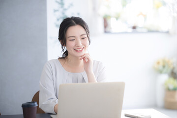 パソコンをしながら考える顎に手を当てるかわいい若い日本人(アジア人）女性 画面を見て迷う