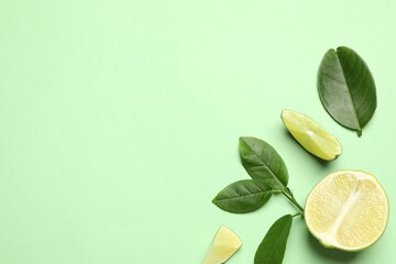 Cut fresh ripe limes with leaves on light green background, flat lay
