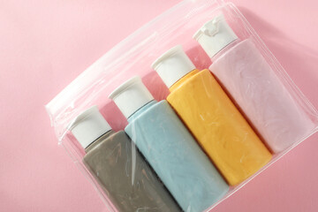 Cosmetic travel kit in plastic bag on pink background, top view