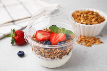 Tasty granola with berries and yogurt in plastic cup on light table, closeup